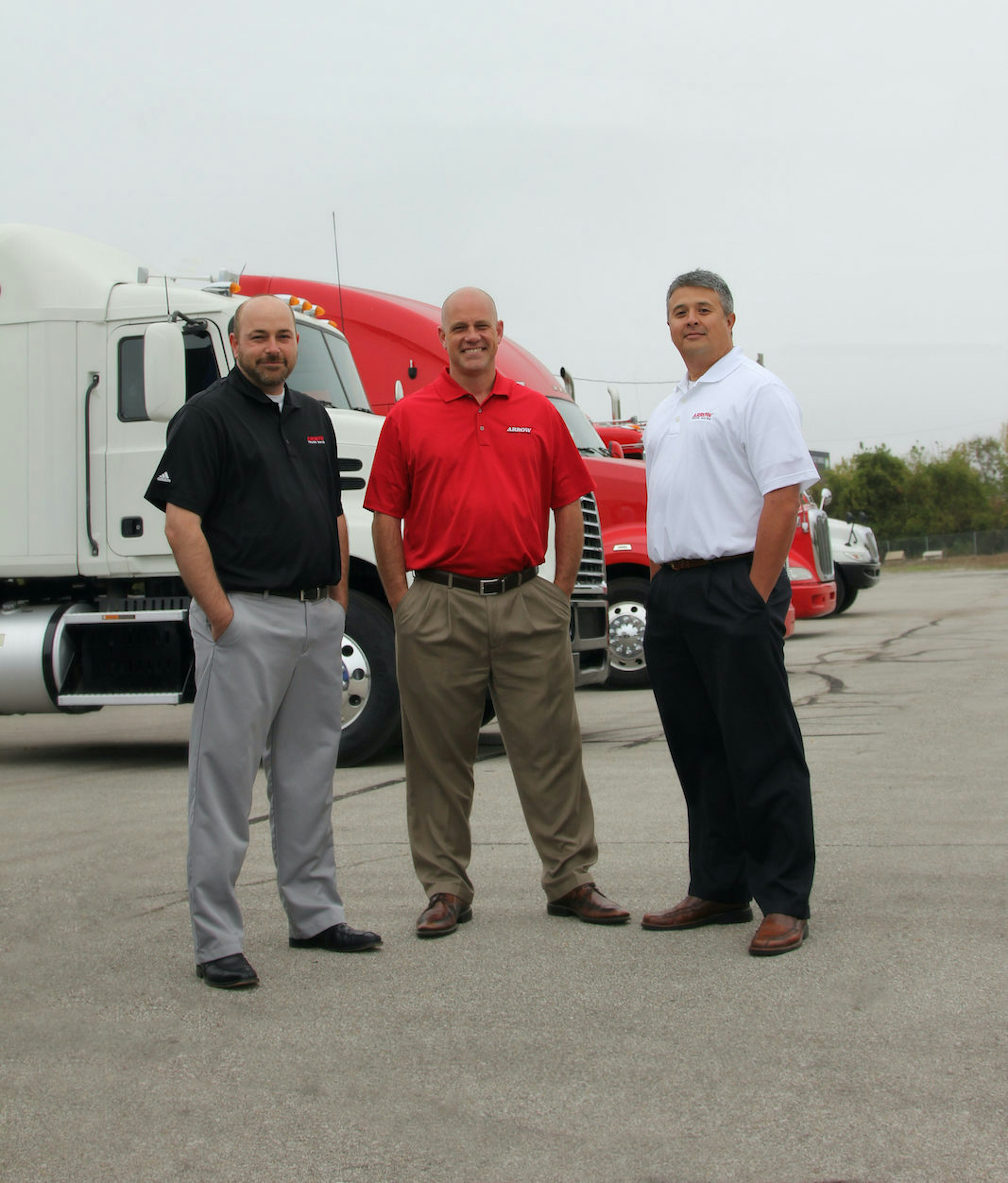 Image of 3 arrow reps standing in front of parked semi trucks. 